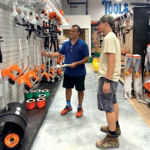 A man helping a customer in a hardware store with lawn equipment